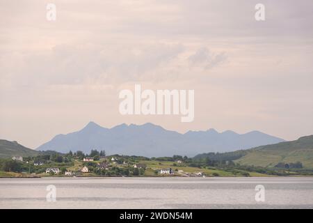 Blick über Loch Portree auf der Isle of Skye in Richtung der Häuser in Heatherfield an einem Sommermorgen mit den Red Cuillin Peaks in der Ferne Stockfoto