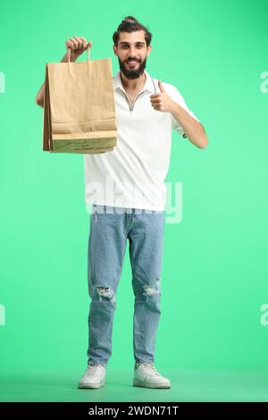 Ein Mann in voller Länge, auf grünem Hintergrund, mit Taschen, zeigt einen Daumen nach oben Stockfoto