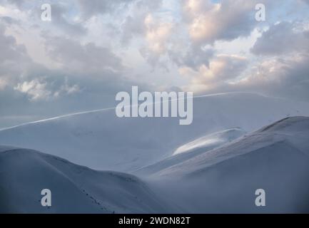 Schneebedeckte Winterberge in letzter Abendsonne. Herrliche windige Dämmerung auf den Gipfeln über dem malerischen alpinen Skigebiet Stockfoto