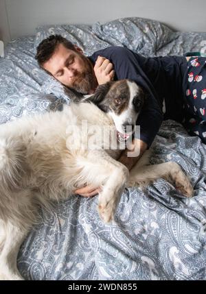 Mann und weißer Hund im Bett Stockfoto