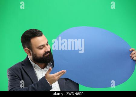 Ein Mann aus der Nähe auf grünem Hintergrund zeigt ein blaues Kommentarzeichen Stockfoto