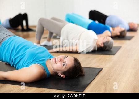 Gruppe junger, reifer alter Menschen in Sportbekleidung, die Pilates während des Liegens auf Matten im Rehabilitationszentrum treiben Stockfoto