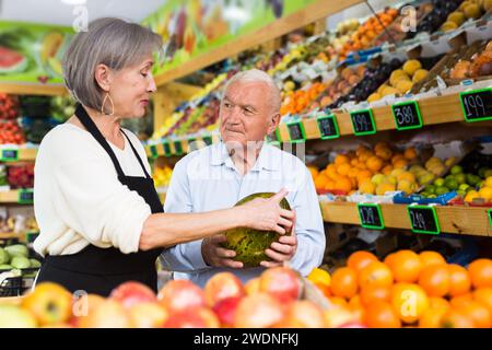 Dame im Gemüsehändler hilft dem alten Mann, Melone zu wählen Stockfoto