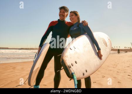 Ein paar Surfer im Wetsuit mit Surfbrettern stehen am Strand und umarmen sich Stockfoto