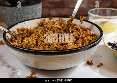 Kochen und Verarbeiten von Pulled Schweinefleisch mit roter Anchochili-Paste und Schweinefleisch auf einem Schneidebrett aus weißem Marmor Stockfoto