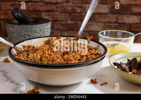 Kochen und Verarbeiten von Pulled Schweinefleisch mit roter Anchochili-Paste und Schweinefleisch auf einem Schneidebrett aus weißem Marmor Stockfoto