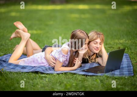 Mutter und Tochter sehen sich im Park gerne einen Laptop an. Stockfoto