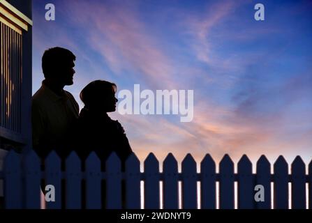 Silhouette eines jungen Paares, das den wunderschönen Sonnenuntergang am Abend mit einem Pflückzaun im Vordergrund beobachtet Stockfoto