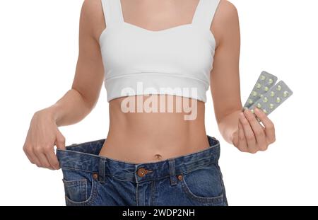 Schlanke Frau in großer Jeans mit Pillen auf weißem Hintergrund, Nahaufnahme. Gewichtsverlust Stockfoto