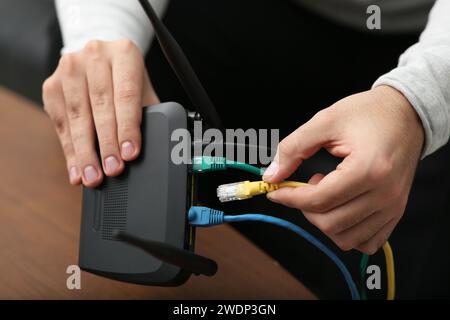 Mann, der Kabel in den WLAN-Router an einem Holztisch drinnen steckt, Nahaufnahme Stockfoto