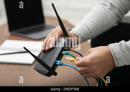 Mann, der Kabel in den WLAN-Router an einem Holztisch drinnen steckt, Nahaufnahme Stockfoto