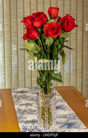 Ein Blumenstrauß aus einem Dutzend roten Rosen in einem Glaseinsatz auf dem Tisch Stockfoto