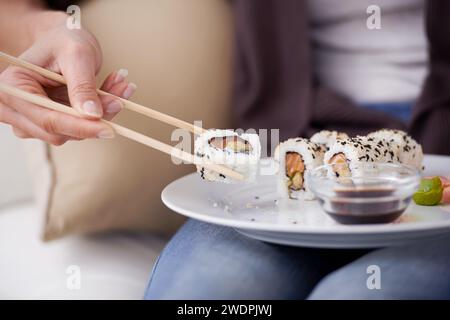 Hände, Sushi-Teller und Essstäbchen zu Hause, Nahaufnahme oder Essen für Wellness, Diät oder Mahlzeit mit Sojasauce. Hungrige Person, Fisch und Gericht zum Mittagessen Stockfoto
