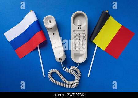 Altes Telefon und zwei Flaggen auf blauem Hintergrund, Konzept zum Thema Telefongespräche zwischen Belgien und Russland Stockfoto