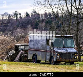 Ein verrosteter Truck, der auf dem Feld mit gestapelten alten Autos geparkt ist Stockfoto