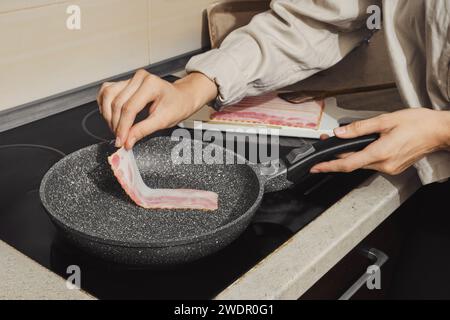 Unerkennbare Frau legte Speck auf heiße Bratpfanne in der Küche Stockfoto