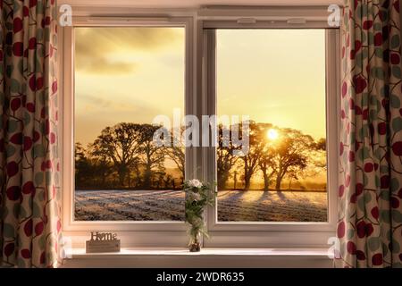 Fenster und ein wunderschöner Blick auf den Sonnenuntergang auf Bäume und Felder in der Abenddämmerung. Fenster geschlossen mit Vorhängen und Stockfoto