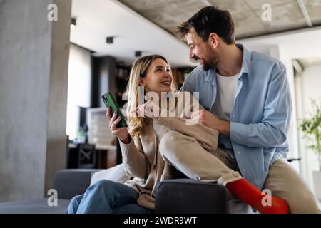 Ein junges glückliches Paar, das zu Hause Nachrichten aus sozialen Medien per Telefon mitteilt und online einkauft. Stockfoto