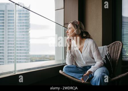 Krankenschwester oder Ärztin genießt nach der Arbeit Freizeit zu Hause, sitzt am Fenster und hört Meditation entspannende Musik. Vereinbarkeit von Beruf und Privatleben im Gesundheitswesen Stockfoto