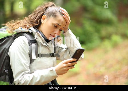 Ein verlorener Wanderer beschwert sich über das Handy, der in einem Wald läuft Stockfoto