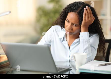 Besorgter schwarzer Telearbeiter, der den Laptop überprüft, der zu Hause arbeitet Stockfoto