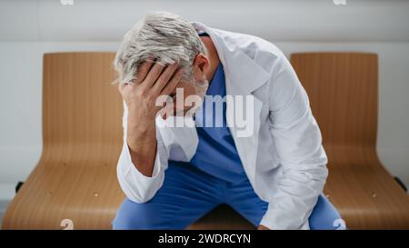 Niedrigwinkelaufnahme eines frustrierten, erschöpften Arztes, der im Krankenhauskorridor sitzt. Das Konzept des Burnout-Syndroms bei Ärzten. Stockfoto