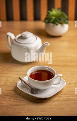 Weißer Teekessel und weiße Tasse mit frischem Tee auf Holztisch Stockfoto