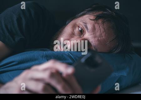 Mann mit Smartphone, während er spät nachts im Bett liegt, Schlaflosigkeit-Konzept, selektiver Fokus Stockfoto