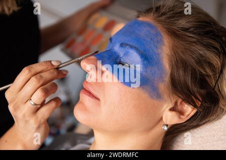 Nahporträt einer Frau, deren Gesicht von einem Künstler mit Pinsel blau gemalt wurde. Kreatives Make-up, leistungsstarkes Make-up Stockfoto