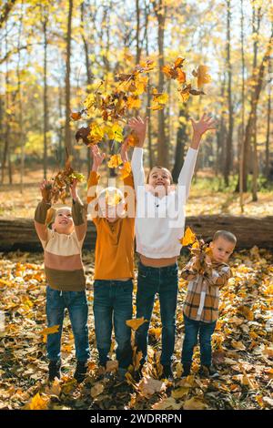 Glückliche Kinder werfen gelbe Herbstblätter in die Luft im Wald Stockfoto