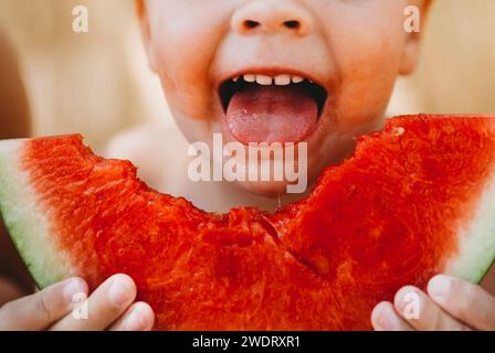 Junge lächelt mit der Zunge heraus und hält Wassermelonenscheibe an heißen Sommertagen Stockfoto