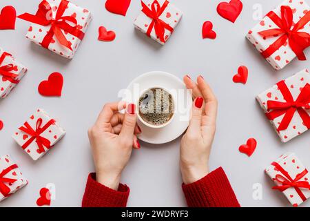 Flache Lage einer herzförmigen Tasse schwarzen Kaffees in den Händen von Frauen auf farbigem Hintergrund mit Kopierbereich Draufsicht. Valentinstag- und Feiertagskonzept. Stockfoto