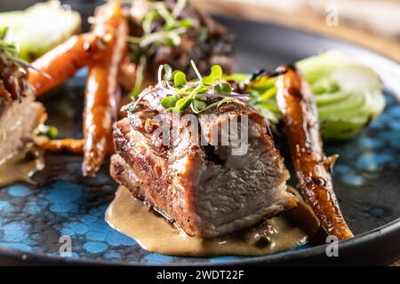 Drei Stücke gebackener Bauch mit gegrilltem Gemüse auf einem Teller in einem Pub oder Restaurant. Stockfoto