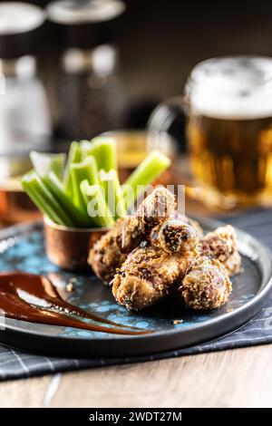 Gebratene Hähnchenschenkel mit Selleriestangen und Bier vom Fass auf Teller im Pub oder Restaurant. Stockfoto