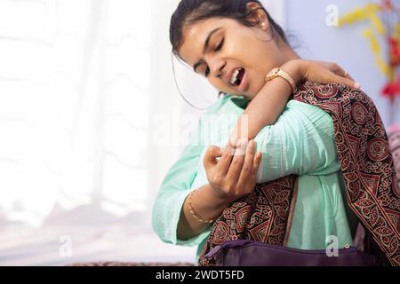 Eine Indianerin, die ihren Ellenbogen wegen Schmerzen hält und drinnen einen schmerzhaften Ausdruck zeigt Stockfoto