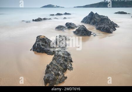 In Sand vergrabene Uferblöcke sehen sich in der Abenddämmerung einer fortschreitenden Flut gegenüber und blicken vom Strand Bantham in Richtung Burgh Island an der Südküste von Devon Stockfoto