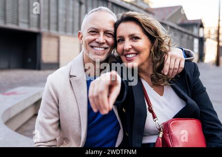 Glückliches, reifes Paar, das sich umschließt und ansieht, wie man zusammen läuft. Liebevoller mittelerwachsener Mann und Frau, die auf der Straße stehen und Arme halten Stockfoto