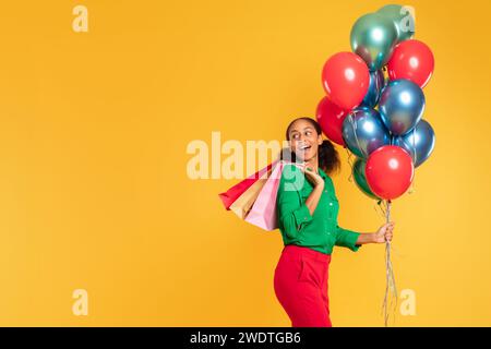 Fröhliches Teenager-Shopper-Mädchen trägt Ballons und Einkaufstaschen, Studio Stockfoto