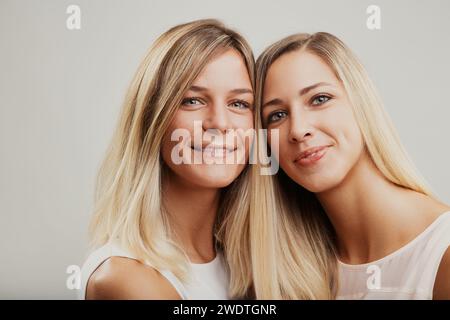 Blonde Frauen, möglicherweise Geschwister, teilen einen fröhlichen Moment, liebevoll in eine Umarmung gehüllt Stockfoto