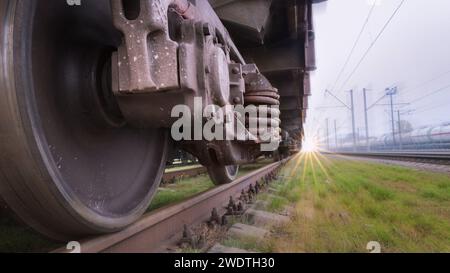 Unteransicht der Räder eines Zuges, der sich schnell auf einer Eisenbahn bewegt. Schnelle Lieferung von Waren auf der Schiene. Ein unscharfer Hintergrund erzeugt einen Bewegungseffekt. Stockfoto