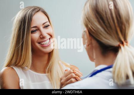 Die sanfte Berührung eines Arztes beruhigt einen lächelnden, optimistischen Patienten. In einem Moment der medizinischen Unterstützung zeigt das dankbare Lächeln einer Frau h Stockfoto