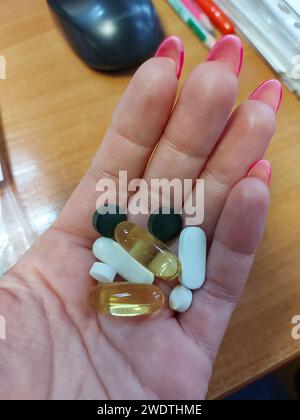 Die Hand hält Omega-3-, Spirulina-, d3-, Biotin- und Magnesiumkapseln. Vitamintabletten am Morgen. Nahrungsergänzungsmittel. Gesundheitsförderung. Biologisch aktive Zusatzstoffe. Stockfoto