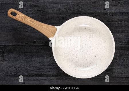 Runde Pfanne auf einem verwitterten schwarzen Holzhintergrund. Antihaftbeschichtete, keramikbeschichtete Kochtechnologie. Stockfoto