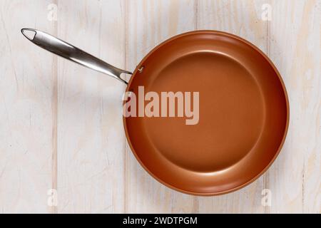 Runde Bratpfanne auf einem verwitterten Hintergrund aus weißem Holz. Antihaftbeschichtete, keramikbeschichtete Kochtechnologie. Stockfoto