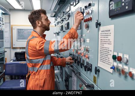 Junger Ingenieur, der in der Motorschaltwarte am Elektroverteilersystem arbeitet, um die Arbeit der elektrischen Generatoren zu synchronisieren. Stockfoto