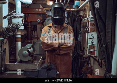 Standporträt der Schweißerin mit Maske und orangenem Overall in der Werkstatt. Stockfoto