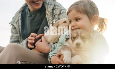 Wunderschönes Porträt einer jungen Frau und ihrer Tochter, beide halten und streicheln ihre neuen Welpen. Freundschaft und Betreuungskonzept Stockfoto