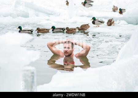 Gutaussehender Junge oder Mann, der im eiskalten Wasser eines gefrorenen Sees zwischen Enten schwimmt. Wim Hof Methode, Kältetherapie, Atemtechniken Stockfoto