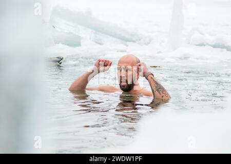 Gutaussehender Junge oder Mann, der im eiskalten Wasser eines gefrorenen Sees zwischen Enten schwimmt. Wim Hof Methode, Kältetherapie, Atemtechniken Stockfoto