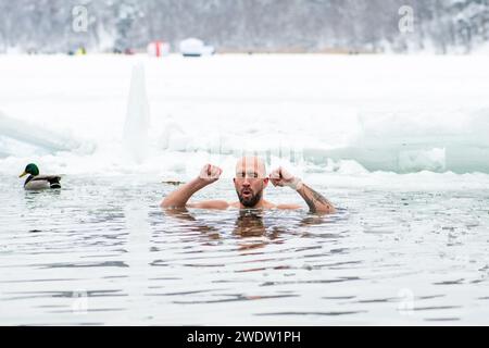 Gutaussehender Junge oder Mann, der im eiskalten Wasser eines gefrorenen Sees zwischen Enten schwimmt. Wim Hof Methode, Kältetherapie, Atemtechniken Stockfoto